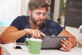 Young Man Eating Breakfast Whilst Using Digital Tablet