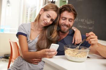 Young Couple Eating Breakfast Whilst Using Mobile Phones