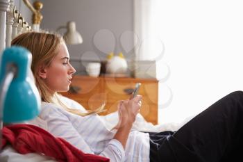 Woman Lying On Bed Whilst Using Mobile Phone