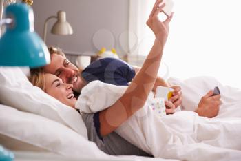 Young Couple Lying In Bed Taking Selfie On Mobile Phone