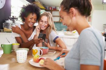 Female Friends Eating Breakfast Whilst Checking Mobile Phone
