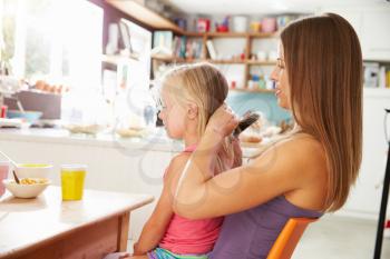 Mother Brushing Daughter's Hair At Breakfast Table