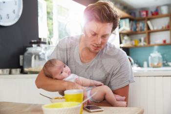 Father With Baby Daughter Checking Mobile Phone In Kitchen