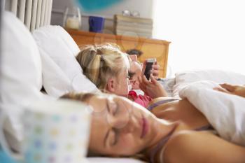 Daughter Plays With Mobile Phone In Bed As Parents Sleep