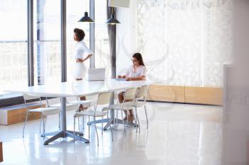 Two women working with digital tablet in empty meeting room