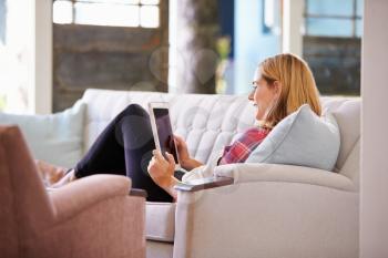 Woman Relaxing On Sofa At Home Using Digital Tablet