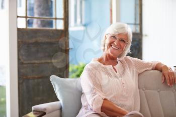 Portrait Of Smiling Senior Woman Sitting On Sofa At Home