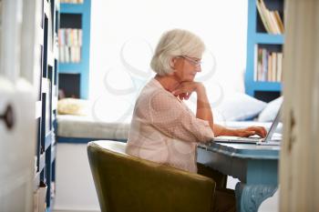Senior Woman At Desk Working In Home Office With Laptop