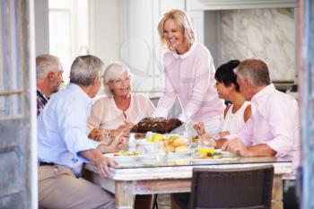 Woman Serving Cake To Group Of Friends Enjoying Meal At Home