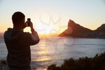 Man Taking Picture Of Sun Setting Over Sea On Mobile Phone