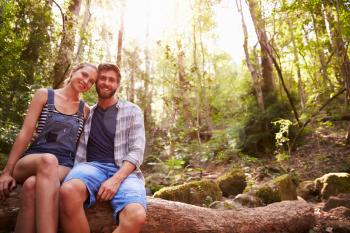 Couple Sitting On Tree Trunk In Forest Together