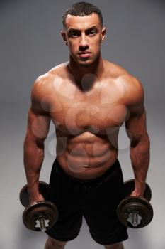 Male bodybuilder holding heavy dumbbells, looking to camera