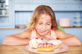 Young Girl Sitting At Table Looking At Plate Of Sugary Cakes
