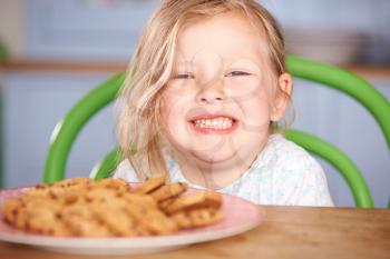 Young Girl Sitting At Table With Plate Of Cookies