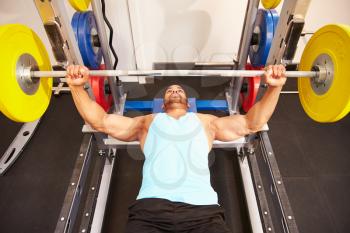 Man flexing muscles while bench pressing weights at a gym