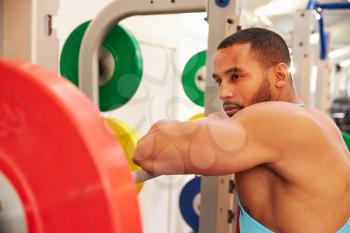 Man leaning on barbells in a rack after weightlifting at gym