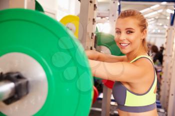 Woman leaning at a squat rack in a gym, smiling to camera