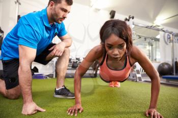 Young woman doing push ups under supervision of a trainer