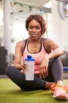 Young woman drinking water in a gym, vertical shot