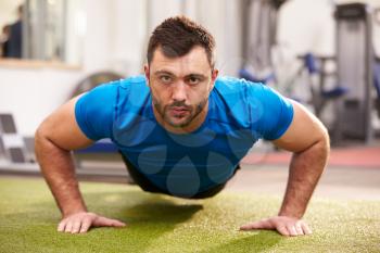 Young man doing push ups at a gym, looking to camera