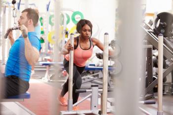 Man and woman exercising using equipment at a busy gym