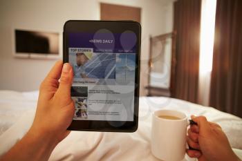 Man In Bed Looking At News Website On Digital Tablet