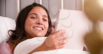 Young Woman Lying In Bed Using Digital Tablet
