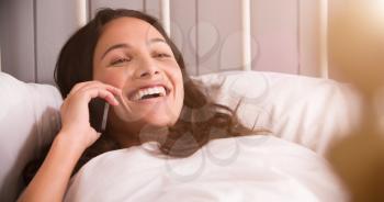 Woman Lying In Bed Having Conversation On Mobile Phone