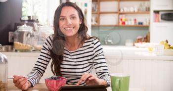 Young Woman Eating Breakfast Whilst Using Digital Tablet