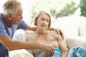 Husband Comforting Senior Woman Feeling Unwell Resting Under Blanket