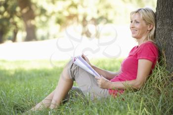 Middle Aged Woman Sketching In Countryside Leaning Against Tree
