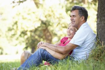 Middle Aged Couple Relaxing In Countryside Leaning Against Tree