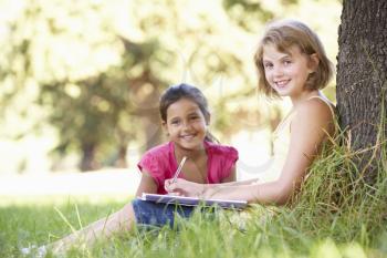 Two Young Girls Sketching In Countryside Leaning Against Tree