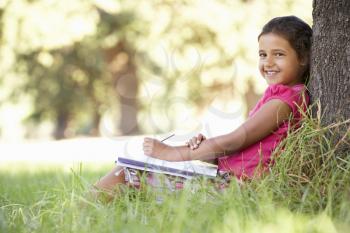 Young Girl Sketching In Countryside Leaning Against Tree