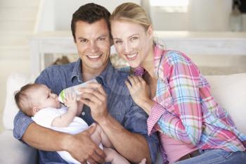 Young Family With Baby Feeding On Sofa At Home