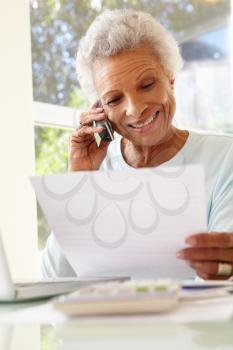 Senior Woman On Phone Using Laptop At Home
