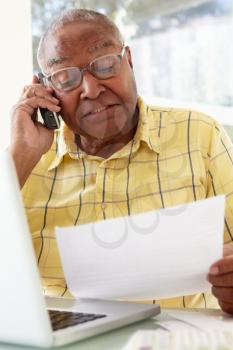 Senior Man On Phone Using Laptop At Home