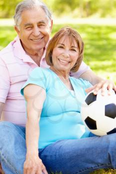 Senior Hispanic Couple Relaxing In Park With Football