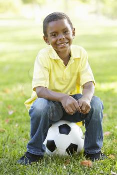 African American Boy Sitting On Football In Park