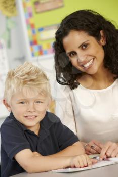 Elementary Age Schoolboy Reading Book In Class With Teacher