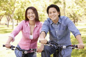 Asian couple riding bikes in park