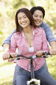 Asian couple both sitting on one bicycle in park