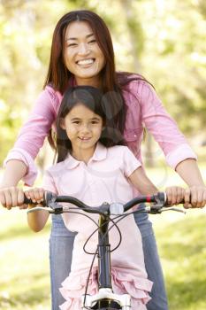 Asian mother and daughter on bicycle in park