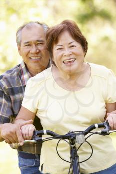 Senior Asian couple both sitting on one bike in park