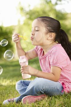 Young Hispanic Girl Blowing Bubbles In Park