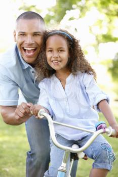 Father Teaching Daughter To Ride Bike In Park