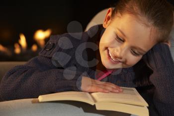 Portrait 7 year old girl reading by firelight
