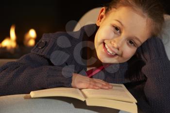 Portrait 7 year old girl reading by firelight