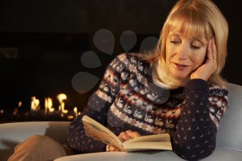 Mature woman reading in front of fire at home