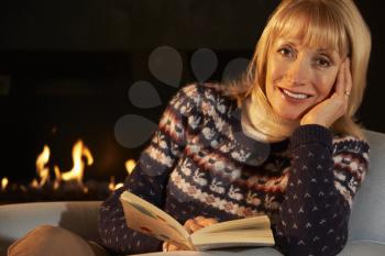 Mature woman reading in front of fire at home